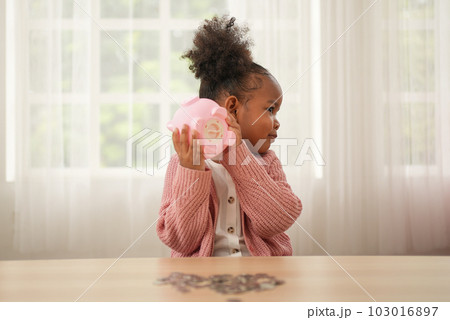 Little girl putting coin of cash into ceramic piggy bank 103016897