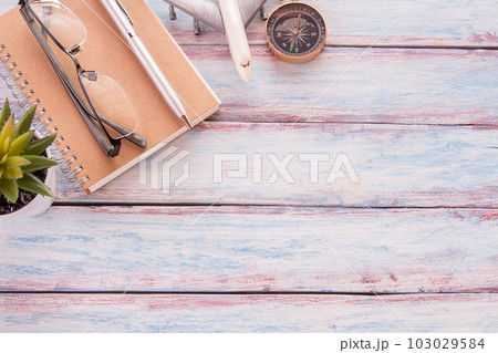 Flat lay photo with notebook,glasses,airplane toy,compass, pen and cuctus flower on wooden table background 103029584