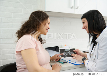 Doctor gynecologist obstetrician consulting her pregnant patient about the ultrasound scan of baby in gynecological clinic. Obstetrics and gynecology. Screening of 1st and 2nd trimester of pregnancy 103034858