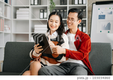 Two asian students learning together online with a laptop, tablet and tutor together in liveing room at home.. 103034860