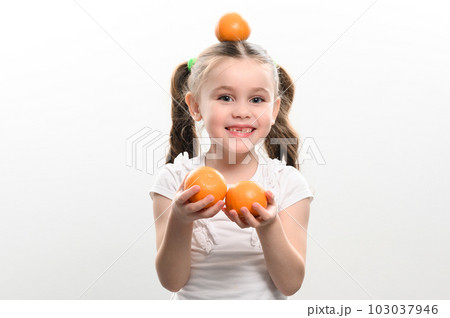 Portrait of a small beautiful girl on a white background with tangerines in her hands. 103037946