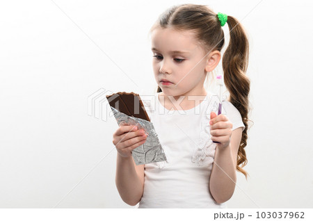A cute little girl is holding a chocolate bar and a toothbrush, a photo idea for dentists and pediatricians. 103037962