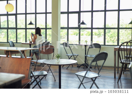 Rear view of woman sits in the coffee shop with empty wooden furniture 103038111