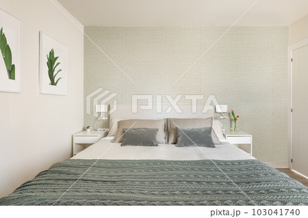 Stylish bright bedroom with bedside tables and a double bed with green beige wallpaper and cute pictures on the wall. The concept of a small but cozy and multifunctional apartment. Copyspace 103041740