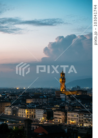 Vertical shot of Old Palace in Florence City Hall tower architect Arnolfo di Cambio in evening lights on warm summer with stunning cumulus clouds. Concept of outstanding architectural structures Vertical shot of Old Palace in Florence City Hall tower architect Arnolfo di Cambio in evening lights on warm summer with stunning cumulus clouds. Concept of outstanding architectural structures 103041744