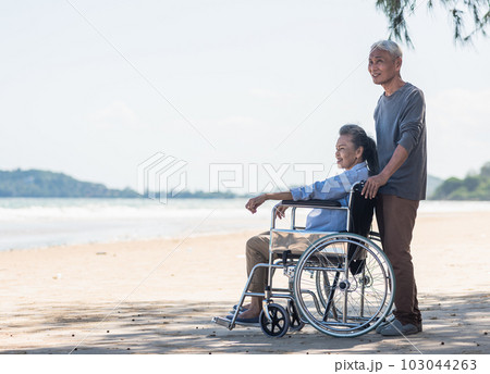 Happy Asian back elderly woman disabled sitting in wheelchair and husband is a wheelchair user on the beach together, summer vacation, Retirement couple concept Happy Asian back elderly woman disabled sitting in wheelchair and husband is a wheelchair user on the beach together, summer vacation, Retirement couple concept 103044263