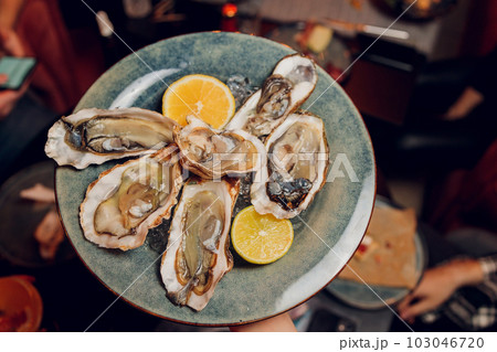 Fresh opened oyster with sliced lemon offered as top view on crushed ice with copy space. Fresh opened oyster with sliced lemon offered as top view on crushed ice with copy space. 103046720