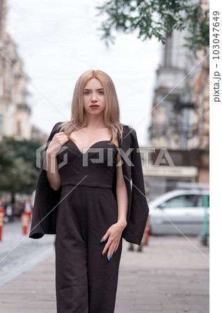 Elegant lady in business suit walks around the city. Young woman is blonde in black suit with deep neckline. Vertical frame. 103047649