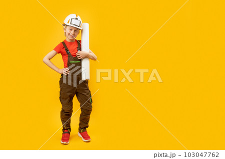 Boy in protective helmet, overalls and with sheet of paper in his hands. Child as builder or architect. Copy space, mockup 103047762