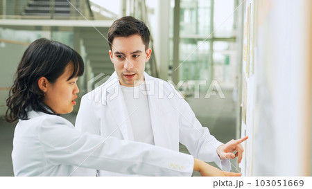研究施設で会話する白衣を着た多国籍グループ 103051669