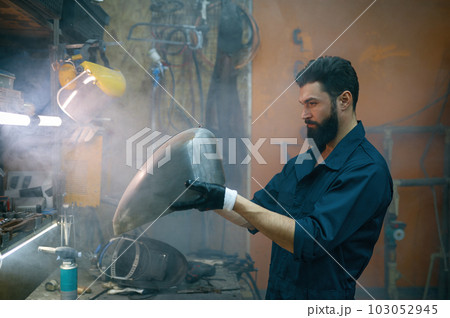 Serious concentrated repairman inspecting new welded part for motorcycle 103052945