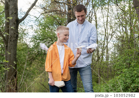 Dad showing paper plane to happy son outdoors, spending time together 103052982
