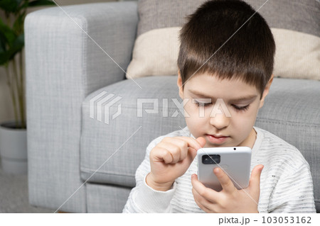 A preschool boy uses a smartphone, plays games on his phone, place for text A preschool boy uses a smartphone, plays games on his phone, place for text 103053162