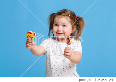 Beautiful little female child holding huge lollipop spiral candy smiling happy isolated on blue background. Beautiful little female child holding huge lollipop spiral candy smiling happy isolated on blue background. 103054124