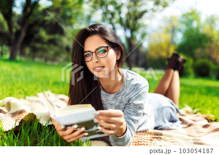 Beautiful relaxed woman readingbook at lawn with sun shining. Girl gets pleasure from reading book. 103054187