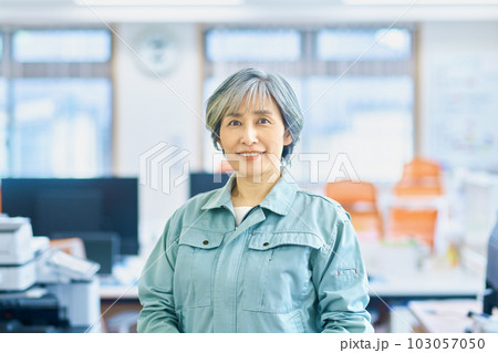 オフィスで並ぶ作業着のシニア女性経営者と若い作業員 オフィスで並ぶ作業着のシニア女性経営者と若い作業員 103057050