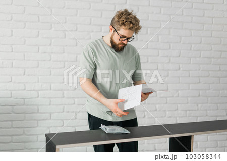 Bearded millennial man assemble his bookcase. He uses tools for furniture. Furniture for the interior room or apartments 103058344