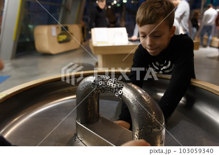 A boy plays with metal objects on a stand with a large magnet 103059340