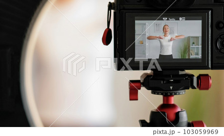 Recording online workout. Sport vlog. Cheerful woman training at home filming creating healthy lifestyle content using camera tripod. 103059969