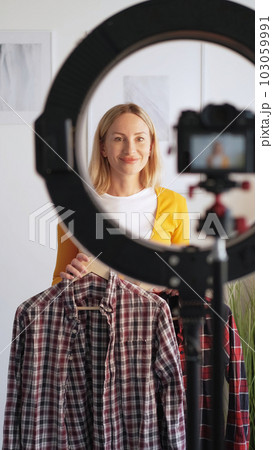 Fashion influencer. Stylist vlogging. Satisfied happy woman recording video blog showing trendy outfit new season filming camera tripod ring light in home interior. 103059991