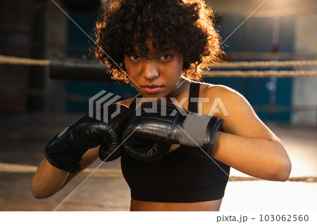 Outcry independent girl power. Angry african american woman fighter with boxing gloves looking serious aggressive standing on boxing ring. Strong powerful fighter girl training punches Outcry independent girl power. Angry african american woman fighter with boxing gloves looking serious aggressive standing on boxing ring. Strong powerful fighter girl training punches 103062560