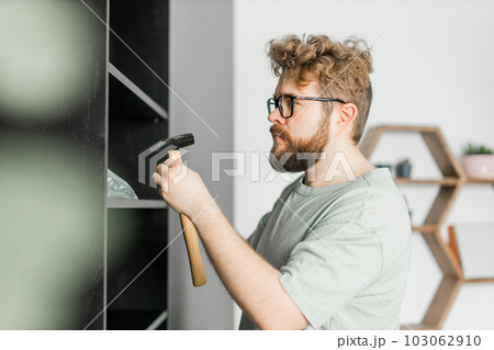 Young attractive man assembles furniture - handwerker and interior objects concept Young attractive man assembles furniture - handwerker and interior objects concept 103062910