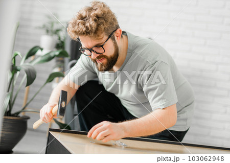 Young attractive man assembles furniture - handwerker and interior objects concept Young attractive man assembles furniture - handwerker and interior objects concept 103062948