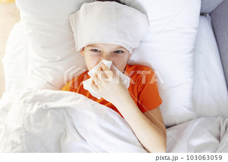 Sick child boy is lying in bed with high fever and blowing his nose Sick child boy is lying in bed with high fever and blowing his nose 103063059