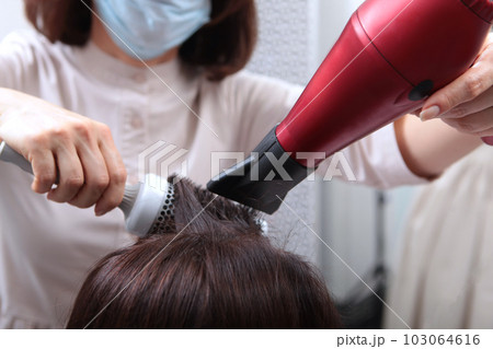Drying long brown hair with hair dryer and a round brush. Close-up. 103064616