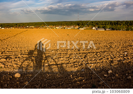 The shadow of a man with a bicycle cast on a plowed field at sunset The shadow of a man with a bicycle cast on a plowed field at sunset 103068809