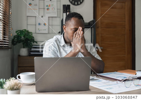 Unhappy hopeless African American man holding head in hands, overwhelmed tired businessman sitting at work desk with laptop, feeling exhausted, financial problem, loss money or bankruptcy 103068847