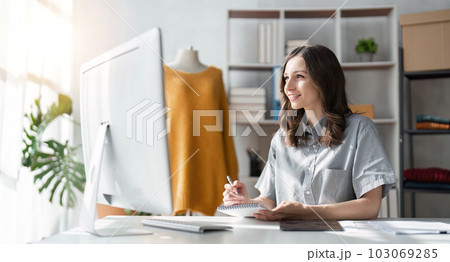 Young attractive female fashion designer sketching idea on paper at desk, working with a laptop at home Young attractive female fashion designer sketching idea on paper at desk, working with a laptop at home 103069285