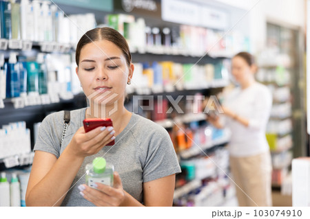 Woman customer using phone to search information about selected product at pharmacy 103074910