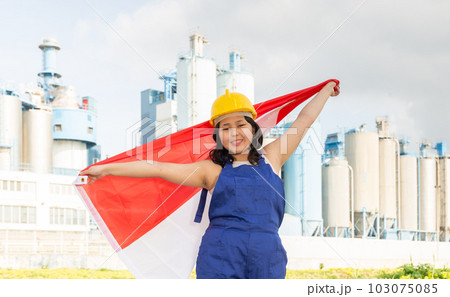Positive girl in overalls with the Indonesia flag in her hands against the background of chimneys of modern factory Positive girl in overalls with the Indonesia flag in her hands against the background of chimneys of modern factory 103075085