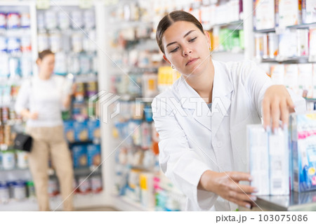 Young female pharmacist arranges product in pharmacy Young female pharmacist arranges product in pharmacy 103075086