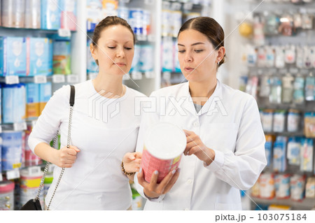 Woman pharmacist helping woman customer choose baby formula in pharmacy 103075184