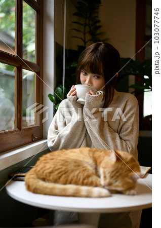 A woman in a cozy sweater resting with her orange cat and sipping tea in living room. A woman in a cozy sweater resting with her orange cat and sipping tea in living room. 103077746