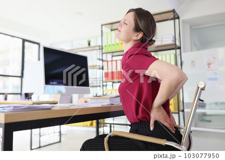 Lady office employee with pain in low back at workplace Lady office employee with pain in low back at workplace 103077950