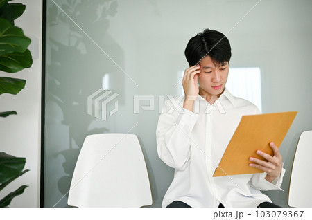 Confused Asian male candidate rechecked his resume while waiting for an interview. 103079367