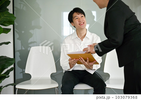 Smiling Asian male candidate talks with a senior businesswoman before an interview. 103079368
