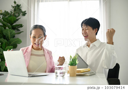 Cheerful senior Asian businesswoman and male employee celebrating their project success Cheerful senior Asian businesswoman and male employee celebrating their project success 103079414