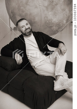 happy smiling man sitting in an armchair in the interior happy smiling man sitting in an armchair in the interior 103087394