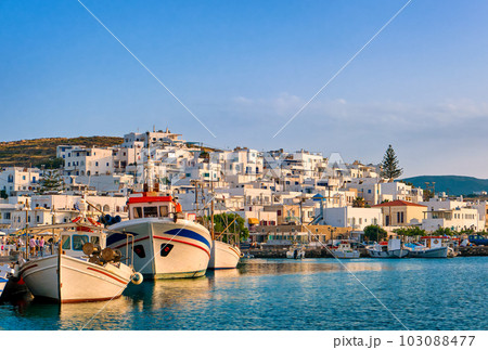 Traditional Greek fishing village and harbour on sunny evening or morning, boats moored by jetty and whitewashed houses alongside. 103088477