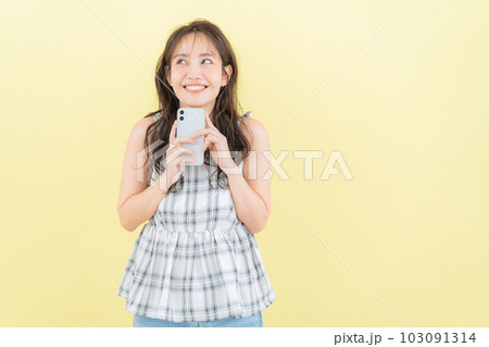 イエローバックでスマホを操作する若い女性 イエローバックでスマホを操作する若い女性 103091314