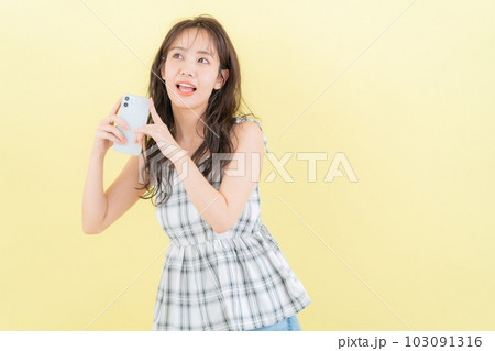 イエローバックでスマホを操作する若い女性 103091316
