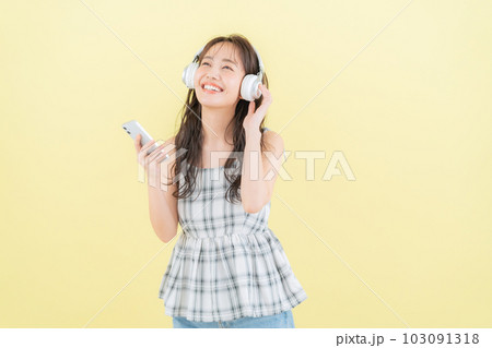 イエローバックでヘッドホンで音楽を聴きながらスマホを操作する若い女性 イエローバックでヘッドホンで音楽を聴きながらスマホを操作する若い女性 103091318