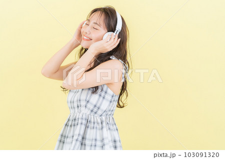 イエローバックでヘッドホンで音楽を聴く若い女性 イエローバックでヘッドホンで音楽を聴く若い女性 103091320