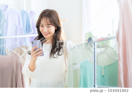 お店でショッピングしながらスマホを操作する若い女性 103091802