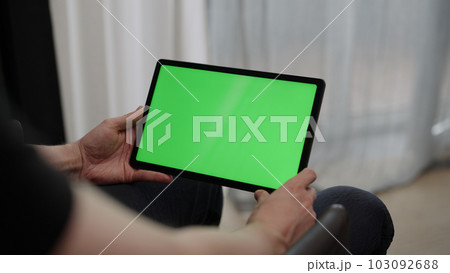 Man sitting indoors on a chair with tablet pc with green screen 103092688