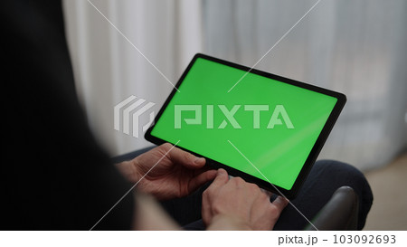 Man sitting indoors on a chair with tablet pc with green screen 103092693